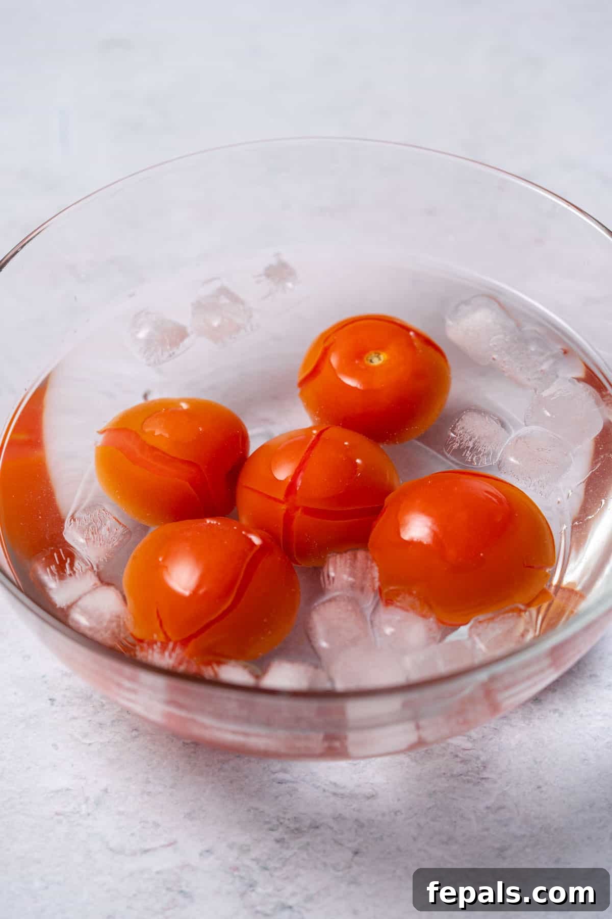 The Simple Trick to Perfectly Peeled Tomatoes 7 Five blanched tomatoes cooling down rapidly in a bowl filled with ice and water, ready for peeling.