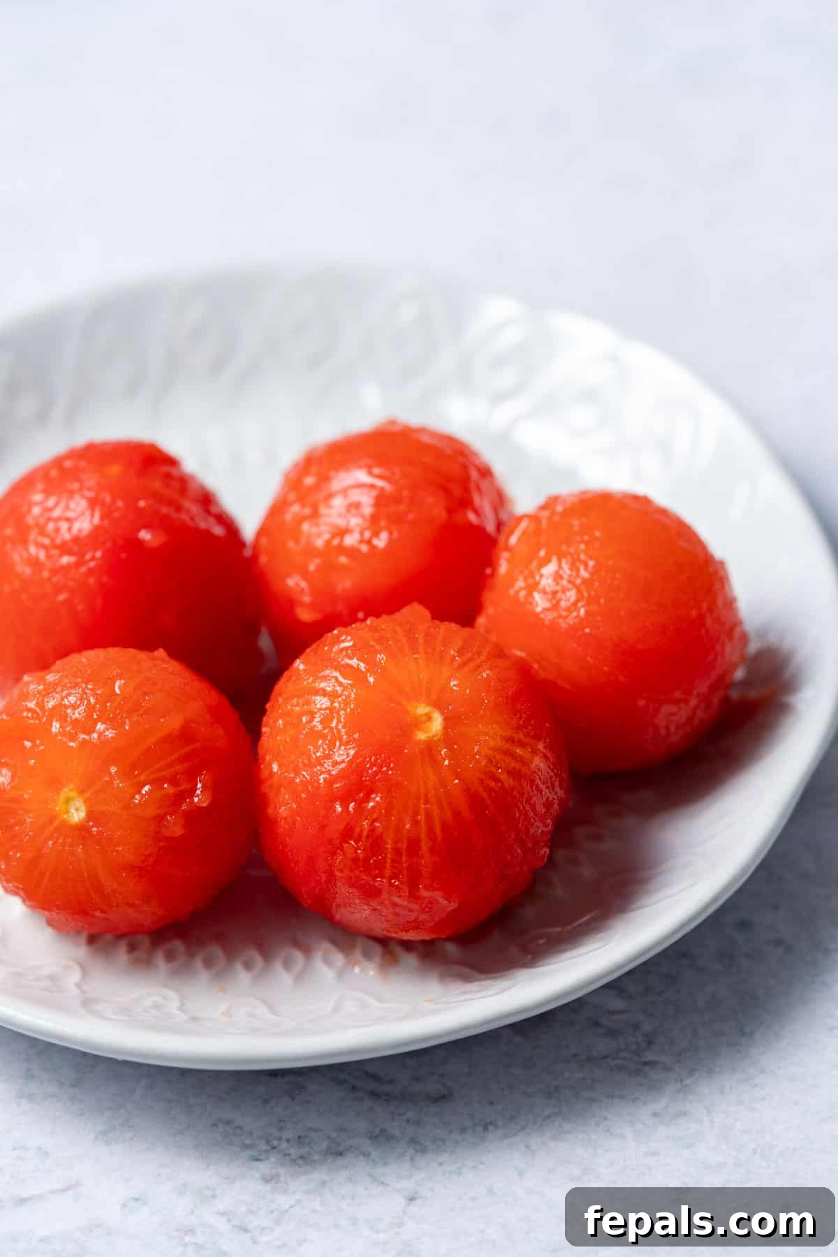 The Simple Trick to Perfectly Peeled Tomatoes 9 A pristine plate displaying five perfectly peeled, ripe red tomatoes, ready for culinary use.