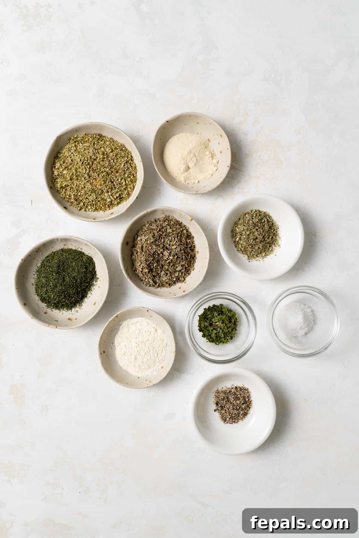 Individual spices and herbs displayed in small bowls, showcasing the components of Greek seasoning