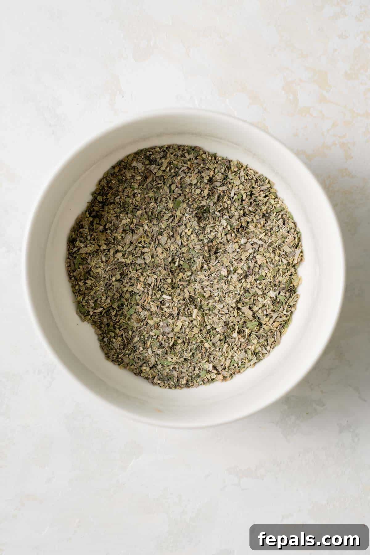 Mixed herbs and spices in a bowl, halfway through combining for Greek seasoning