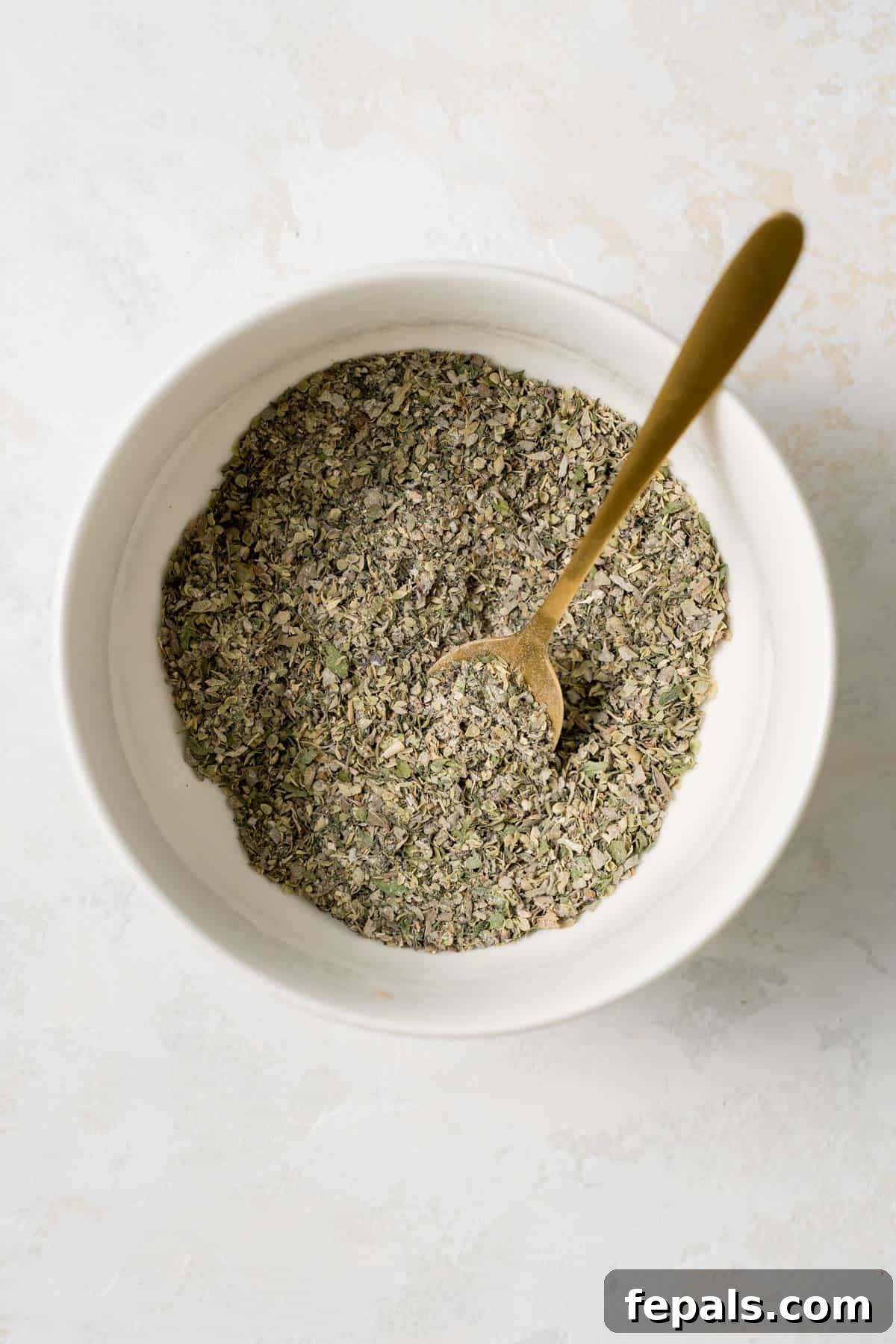 Fully mixed Greek spices and herbs in a bowl with a spoon, ready for storage
