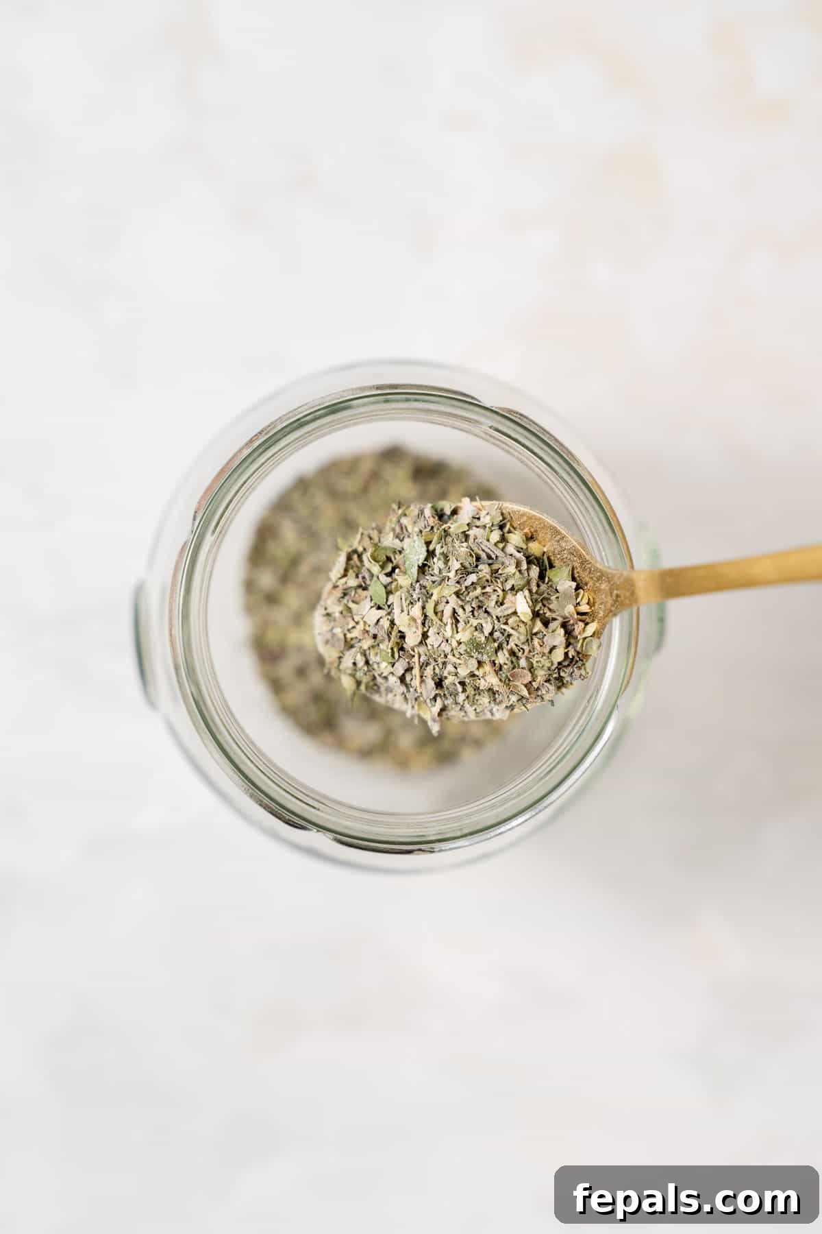 Spoonful of Greek seasoning held above an empty storage jar