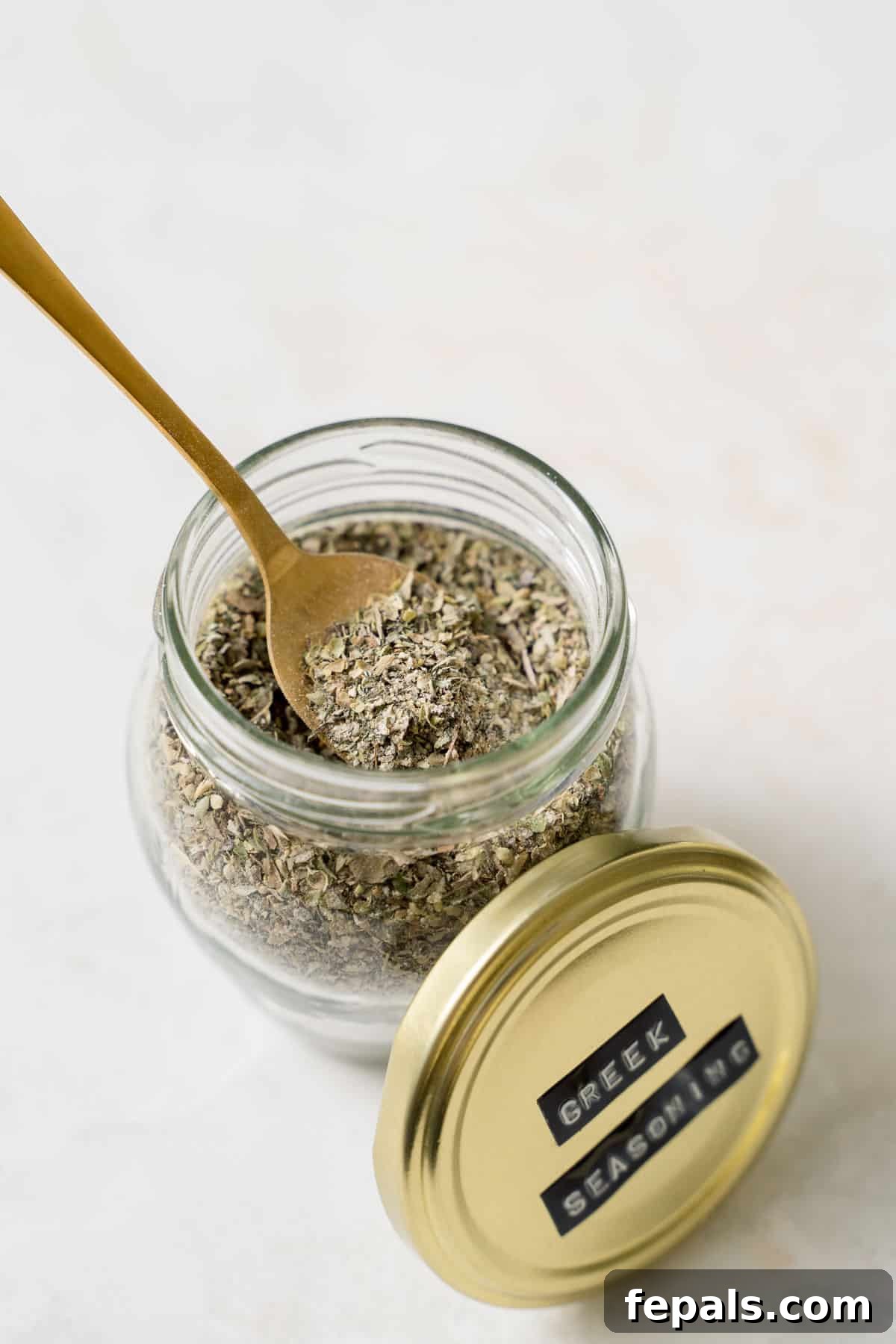A beautiful jar filled with homemade Greek spice blend, with a spoon resting inside