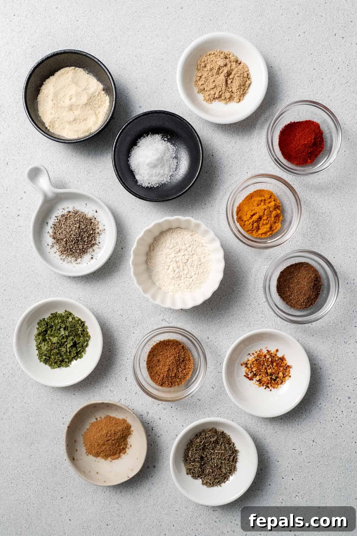 Jerk Seasoning Mix Bowls of onion powder, garlic powder, cayenne, ginger, allspice, coconut sugar, paprika, salt, pepper, hot pepper flakes, cinnamon, parsley, and thyme, ready to be blended into homemade jerk seasoning.