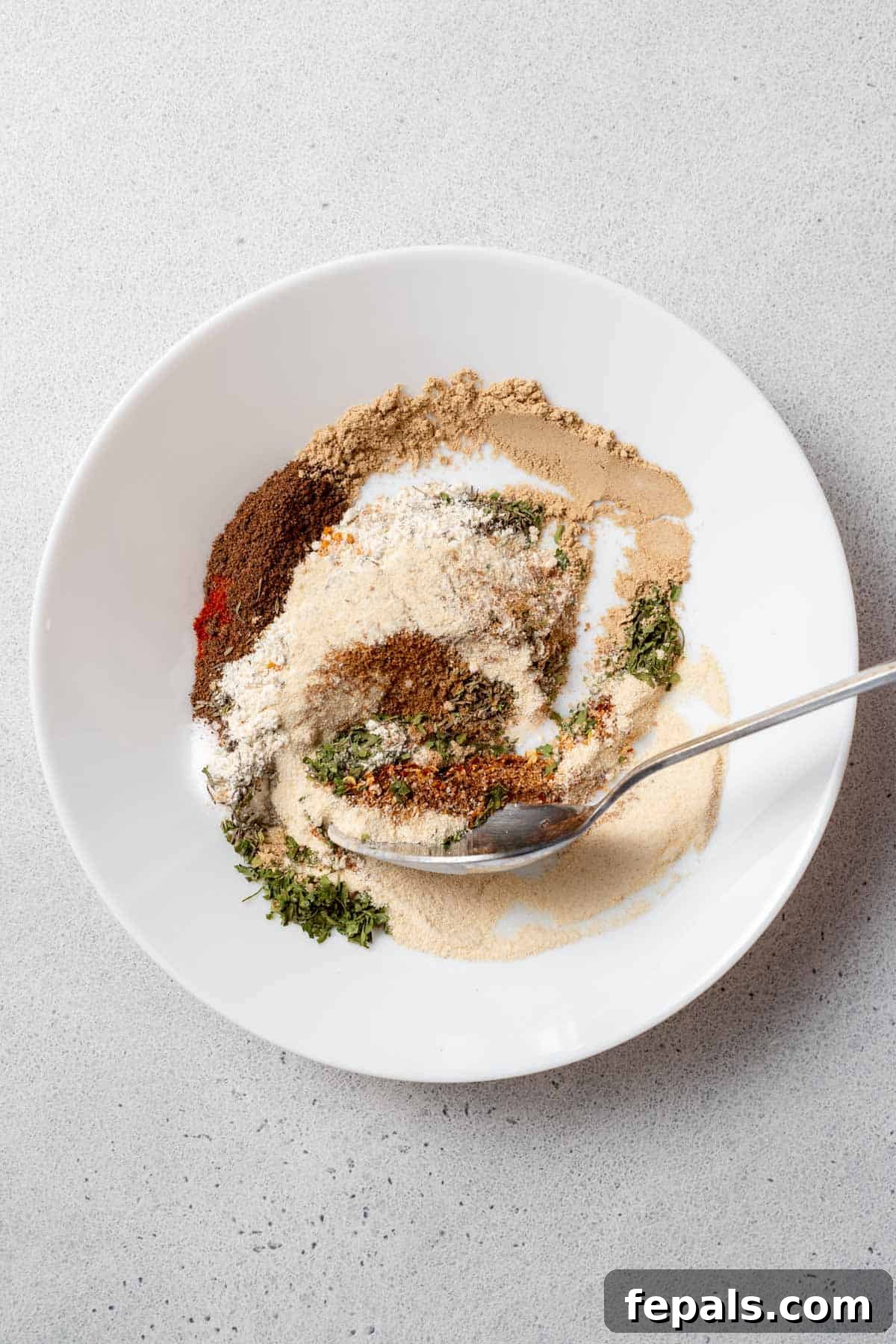 DIY Jerk Seasoning Mix A spoon mixing various spices and herbs in a bowl to create a homemade jerk spice blend.