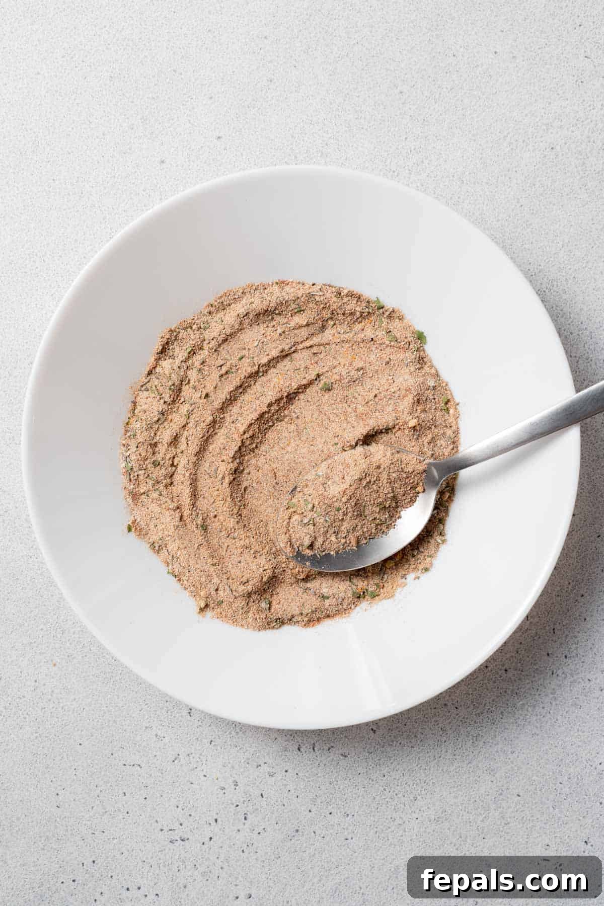 How To Make Jerk Seasoning Mixing spices and herbs vigorously in a bowl with a spoon, ensuring an even blend for jerk seasoning.