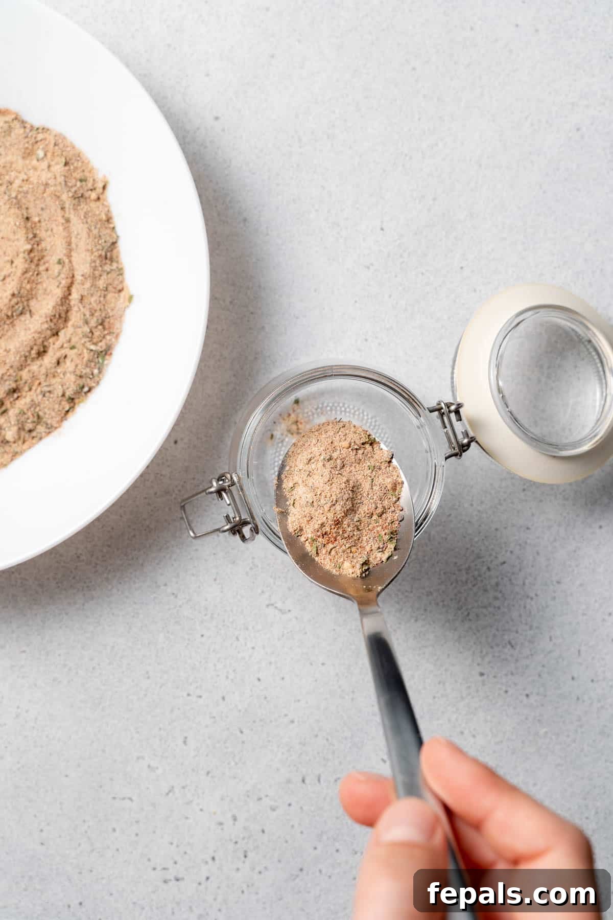 How To Make Jerk Seasoning A spoonful of homemade jerk seasoning being carefully poured into a glass jar for storage.