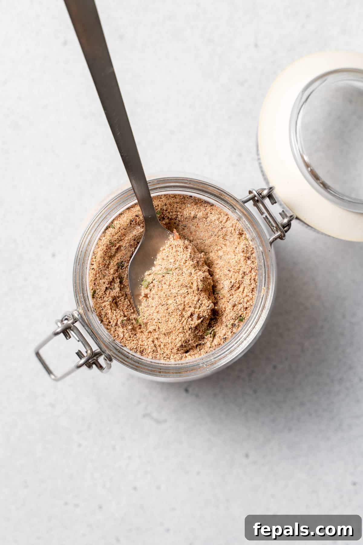 How To Make Jerk Seasoning A jar of homemade jerk seasoning mix, with a small spoon resting inside, ready for use.