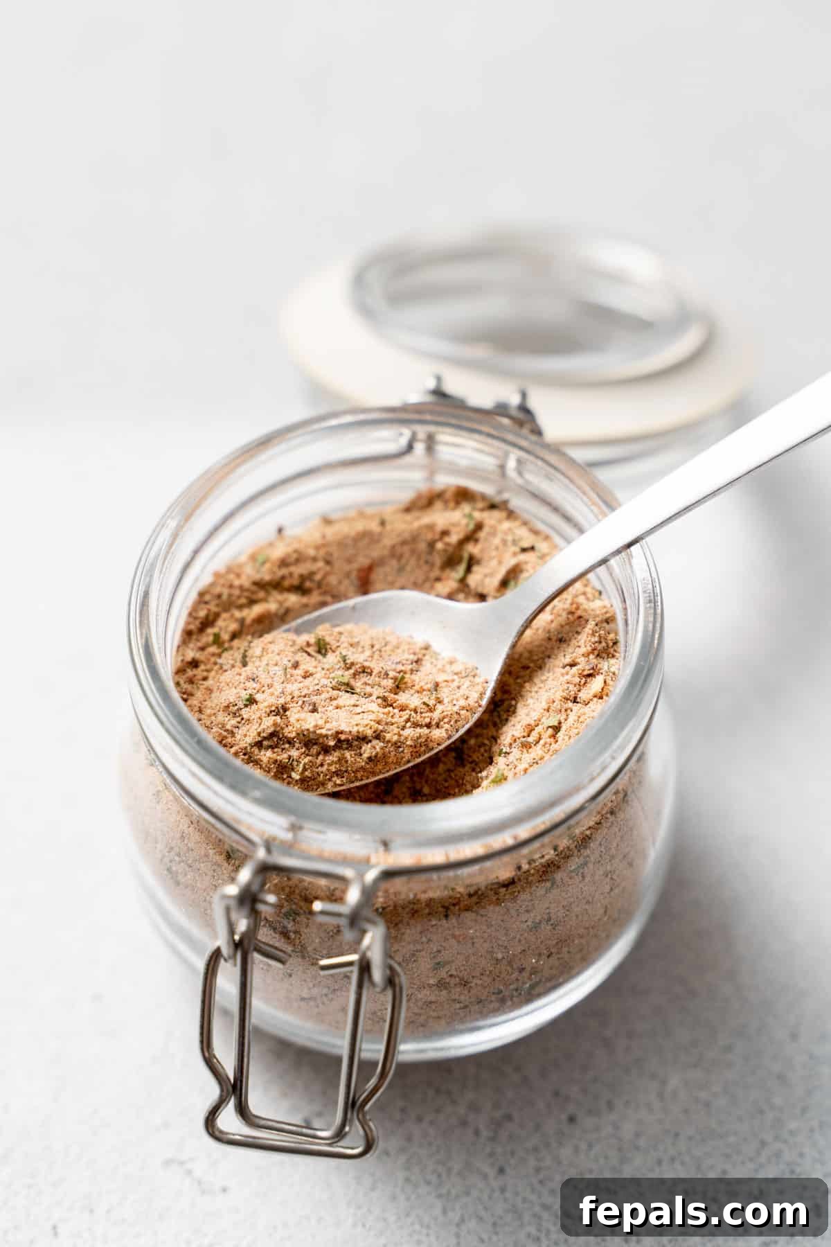 Jerk Spice Mix A clear glass jar, viewed from the side, showcasing the rich color and texture of homemade Jamaican spice mix.