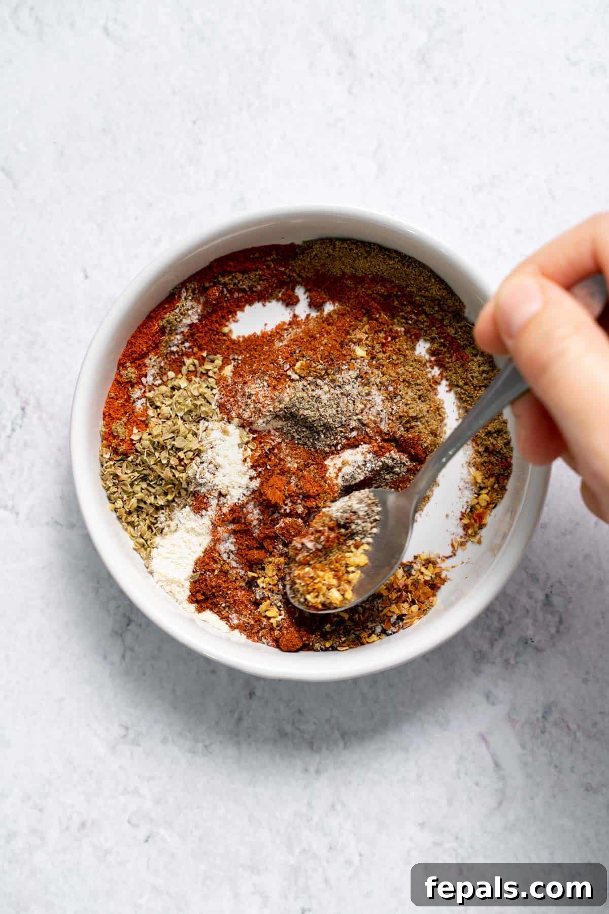 Homemade Taco Seasoning mixing ground spices in bowl with spoon for DIY taco seasoning