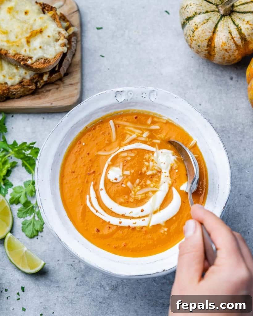 A hand holding a spoon dipped into a bowl of creamy butternut squash soup, ready for a taste.