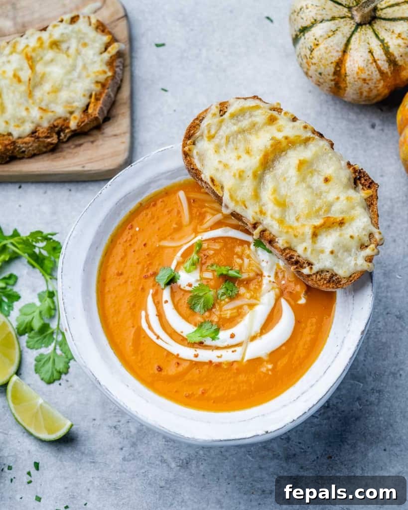 Top view of butternut squash soup in a white bowl, garnished with a sprig of rosemary and served with toast.