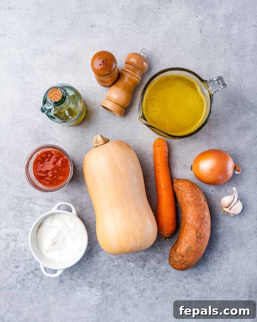 A flat lay image showing all the fresh ingredients needed to make homemade butternut squash soup, including a whole butternut squash, carrots, sweet potatoes, and garlic.