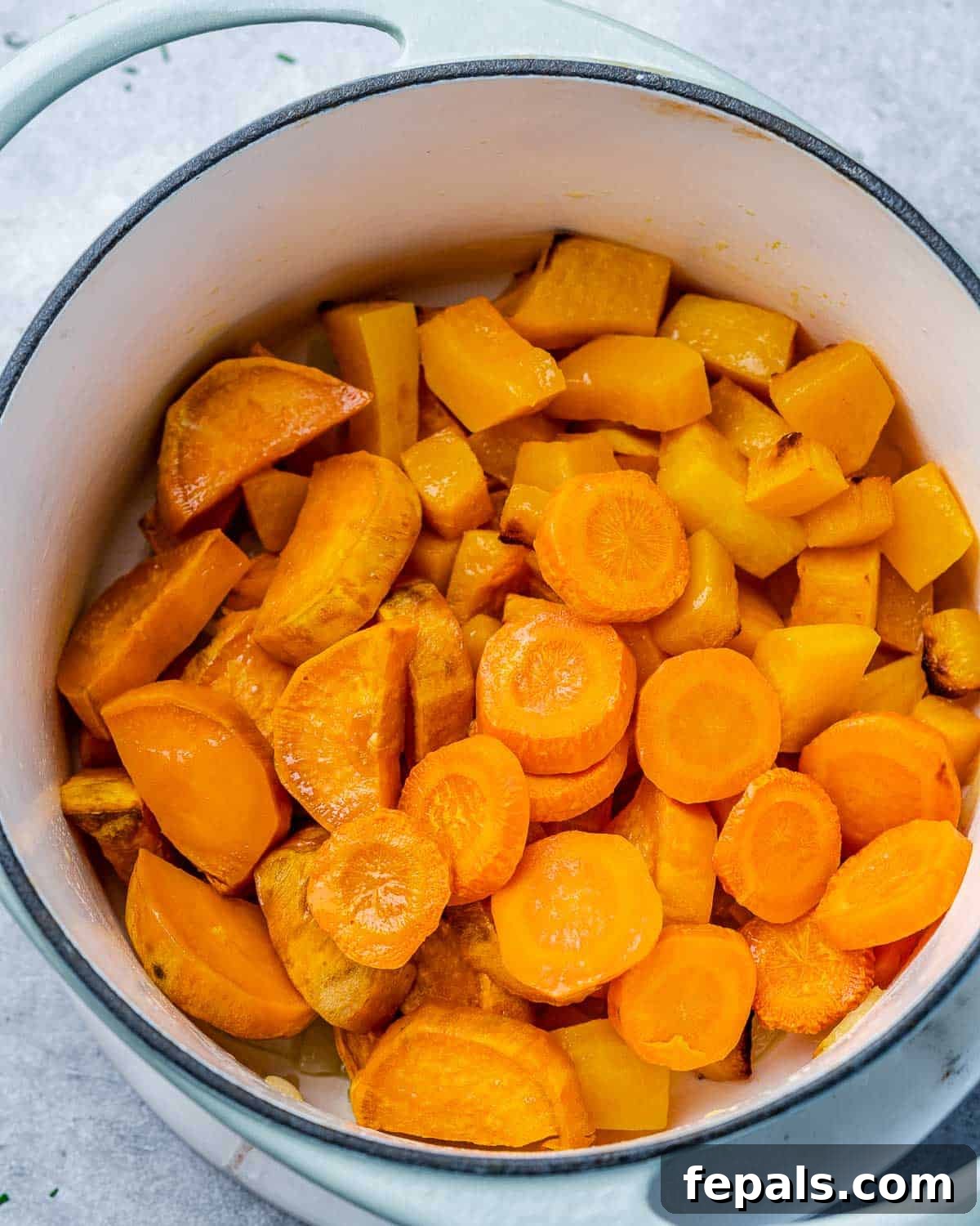 Roasted carrots, sweet potatoes, and butternut squash cubes are combined in a large soup pot with sautéed onions and garlic.