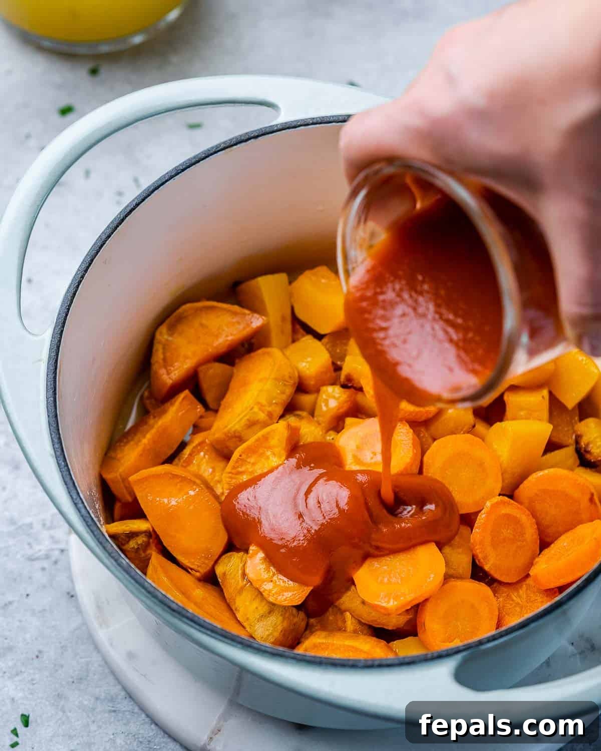 Enchilada sauce is being poured over the roasted vegetables and broth in the soup pot, adding a unique flavor to the butternut squash soup base.