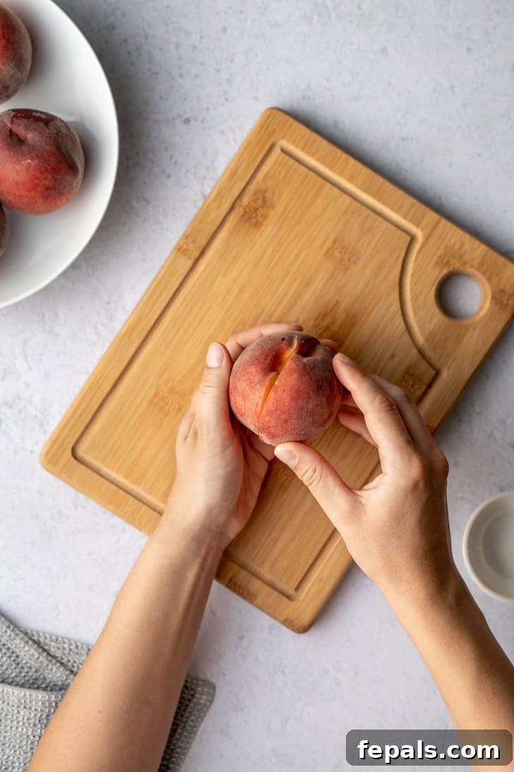 Two hands are carefully pulling a peach apart into two distinct halves, revealing the fruit's juicy interior.