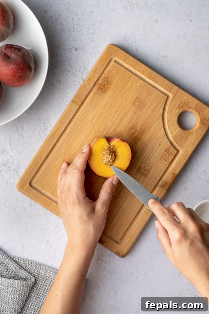 A knife is used to carefully remove the pit from a peach half, highlighting the delicate technique required to preserve the fruit's flesh.