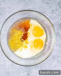Wet ingredients including yogurt, egg, lemon juice and zest, oil, and honey prepared in a clear round bowl before mixing.