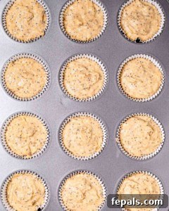 Muffin batter being carefully added to a muffin pan lined with paper cups, ready for baking.