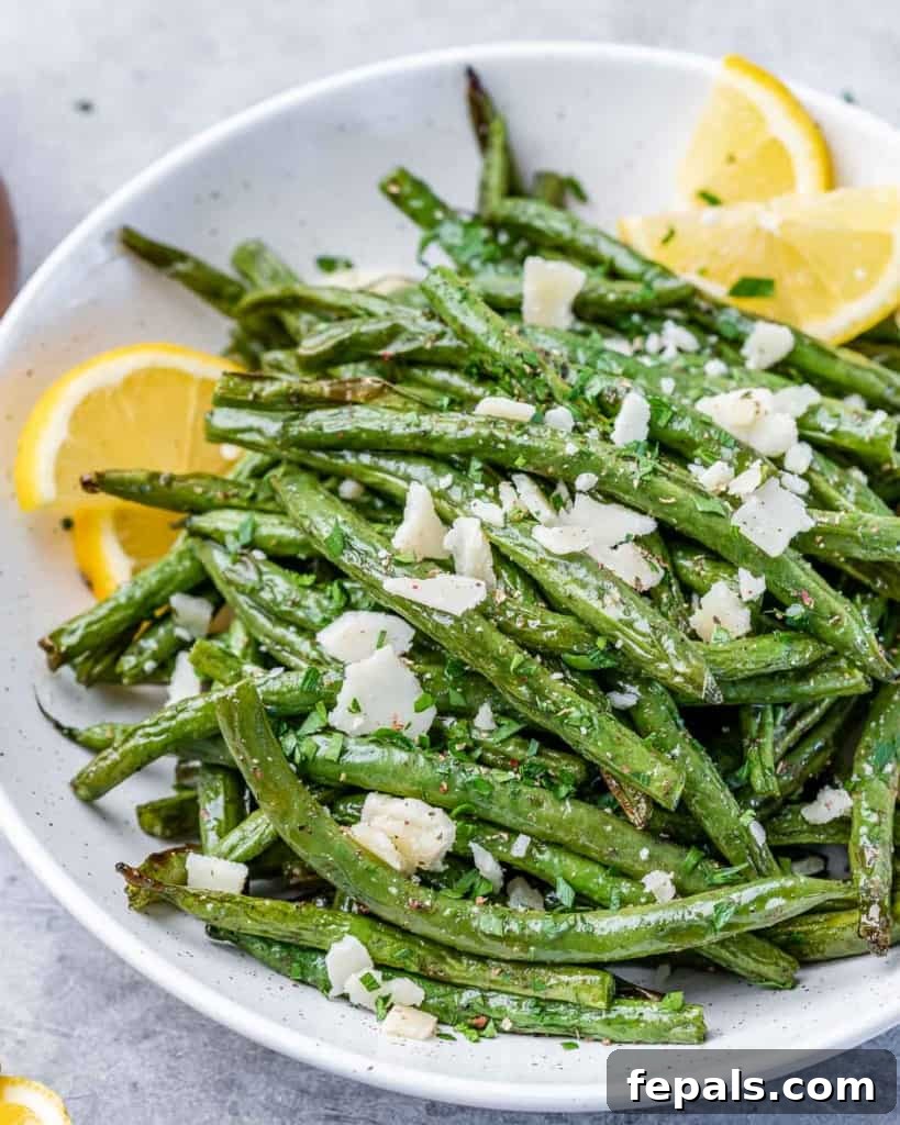 side shot of cooked green beans topped with shaved cheese and lemon wedges