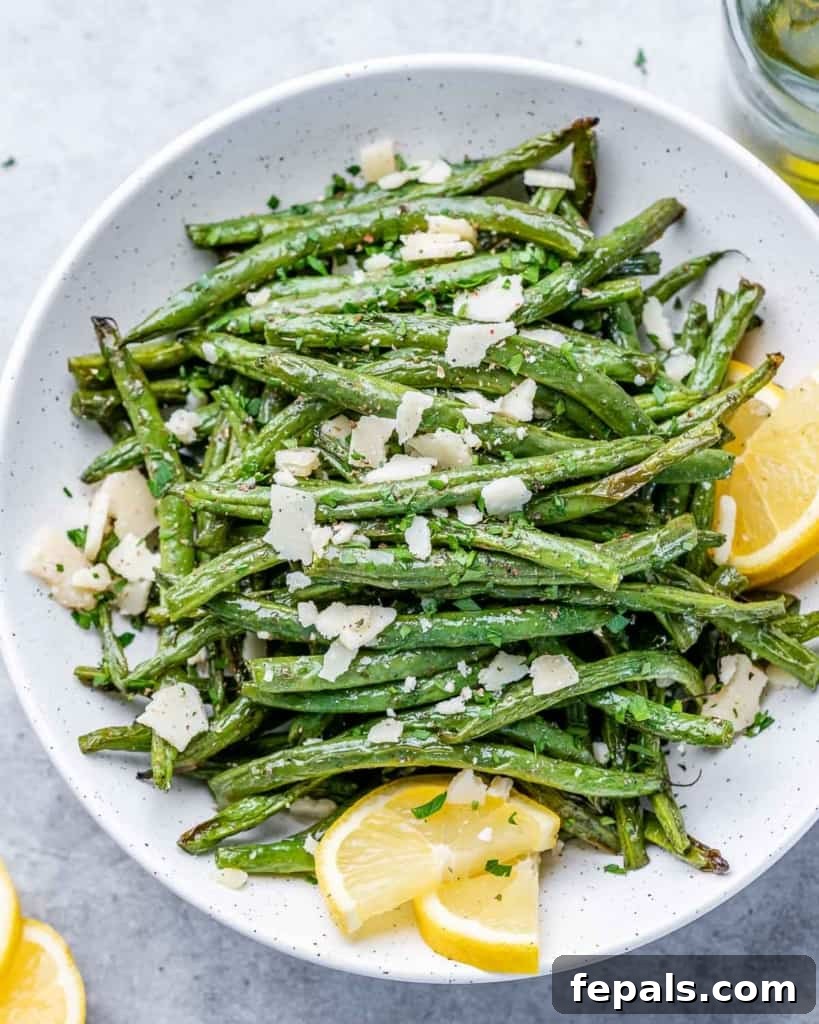 top view cooked green beans topped with shaved parmesan in a round white plate