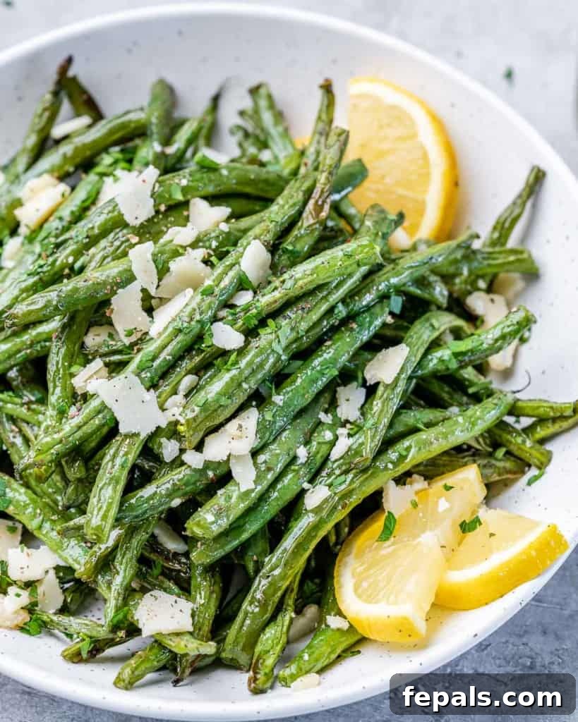 side shot of fried green beans on a white plate with lemon wedged 
