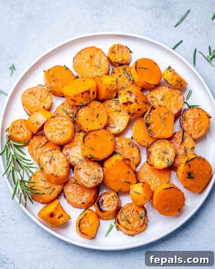 Caramelized Sweet Potatoes 2 Golden brown roasted sweet potatoes on a white plate, garnished with a sprig of fresh rosemary.