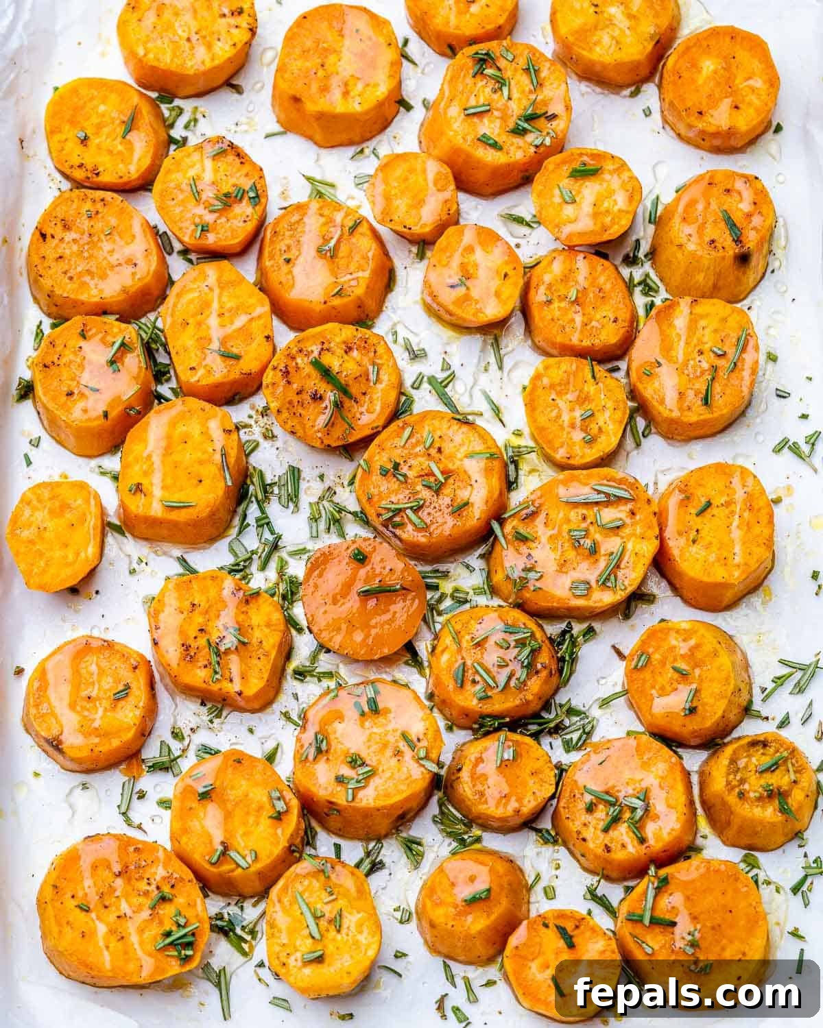 Caramelized Sweet Potatoes 7 Sweet potato rounds drizzled with honey and garnished with fresh rosemary on a baking pan, ready for final roasting.
