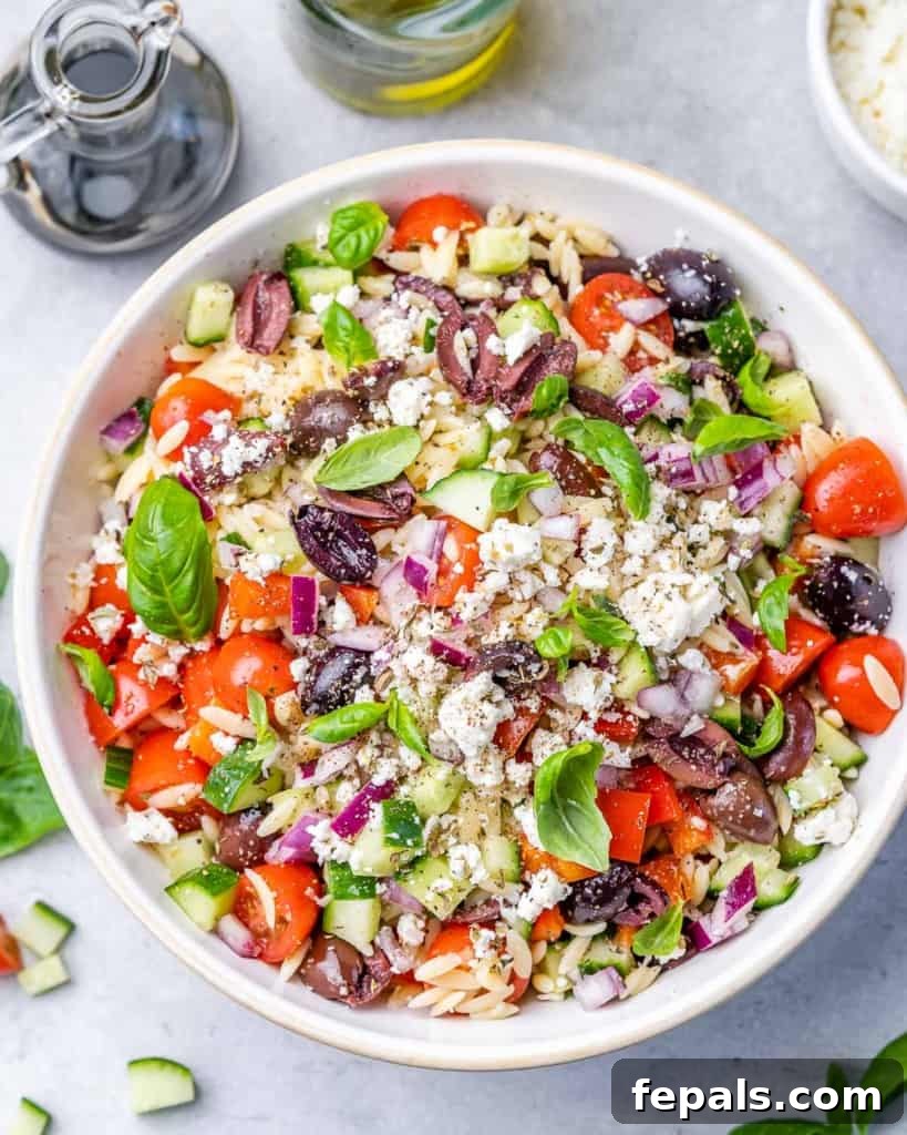 Zesty Greek Orzo Salad 2 Large white serving bowl filled with Greek Orzo Pasta Salad, featuring small pasta, chopped vegetables, and feta cheese.