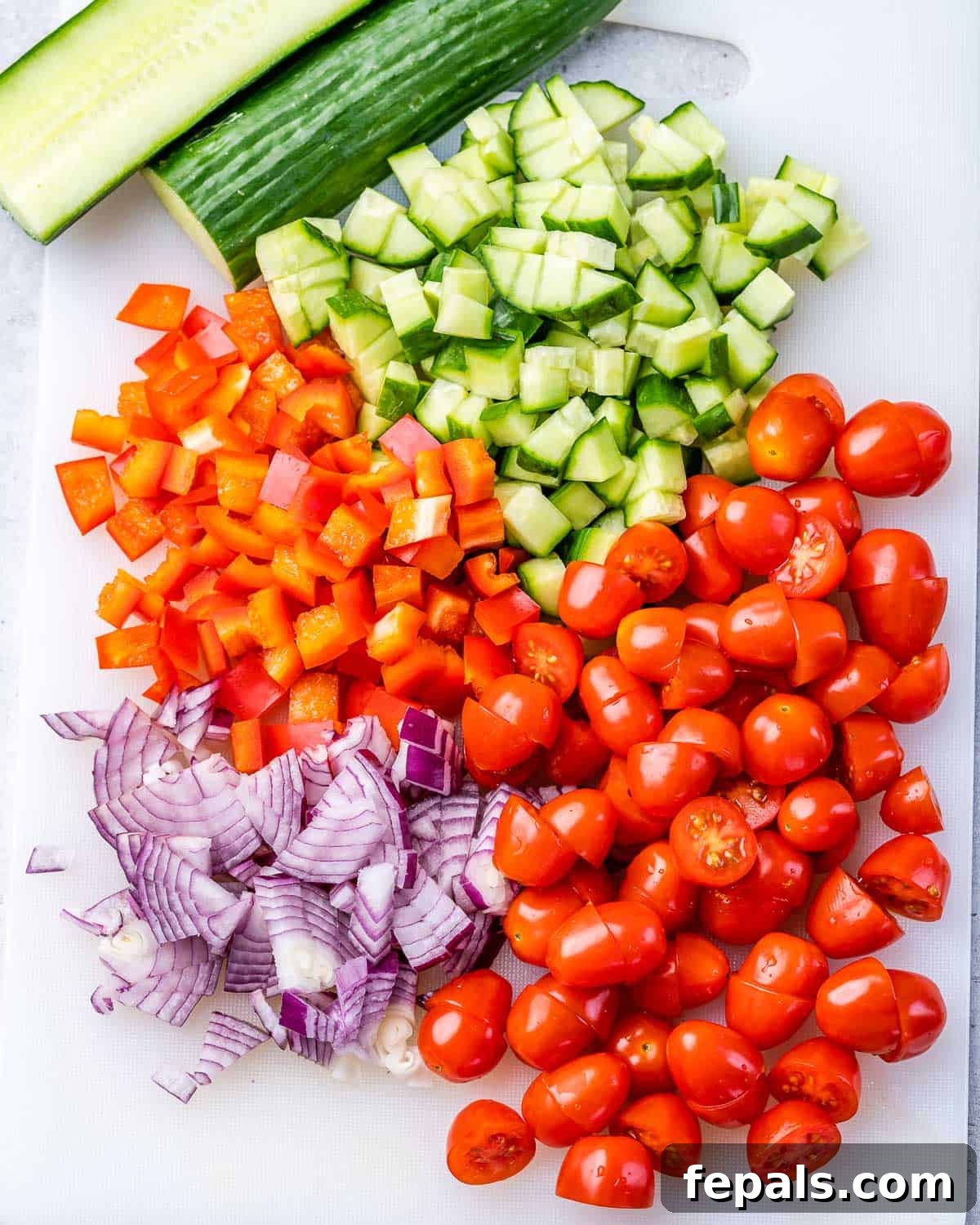 Zesty Greek Orzo Salad 6 Freshly chopped tomatoes, bell pepper, red onion, and cucumber arranged on a cutting board.