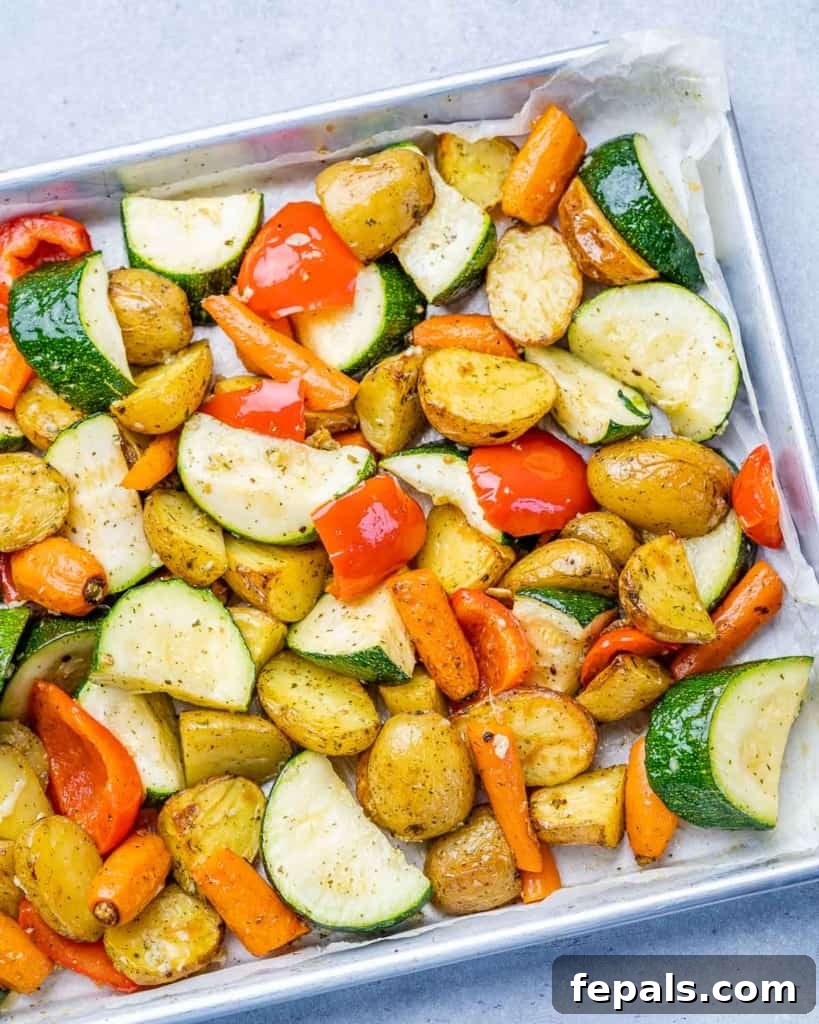 Potatoes roasted with carrots and zucchini on a pan, close up.