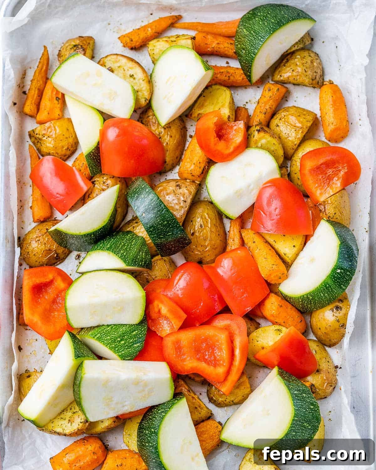 Adding zucchini and bell pepper with partially roasted potatoes and carrots on a baking pan.