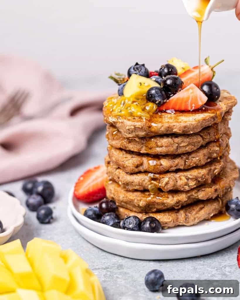 Stack of vegan pancakes topped with maple syrup and fresh fruit.
