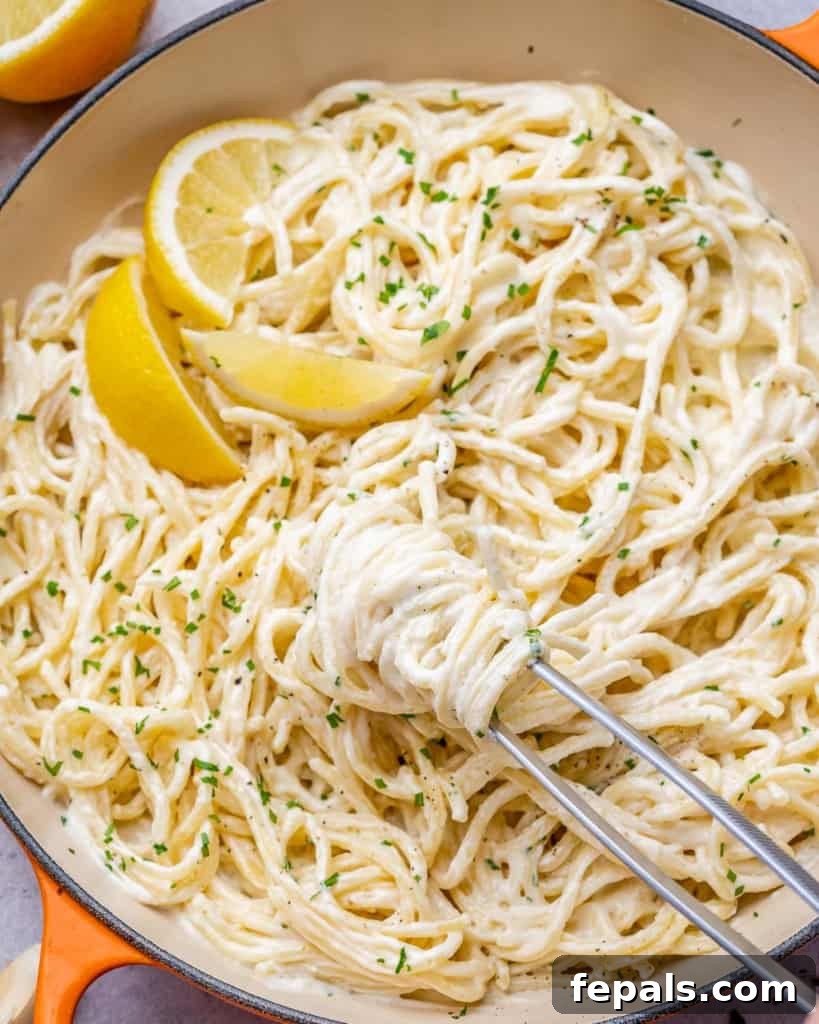 Luscious Vegan Lemon Pasta 11 Tong grabbing a generous portion of lemon pasta from a skillet, showcasing its appealing texture.