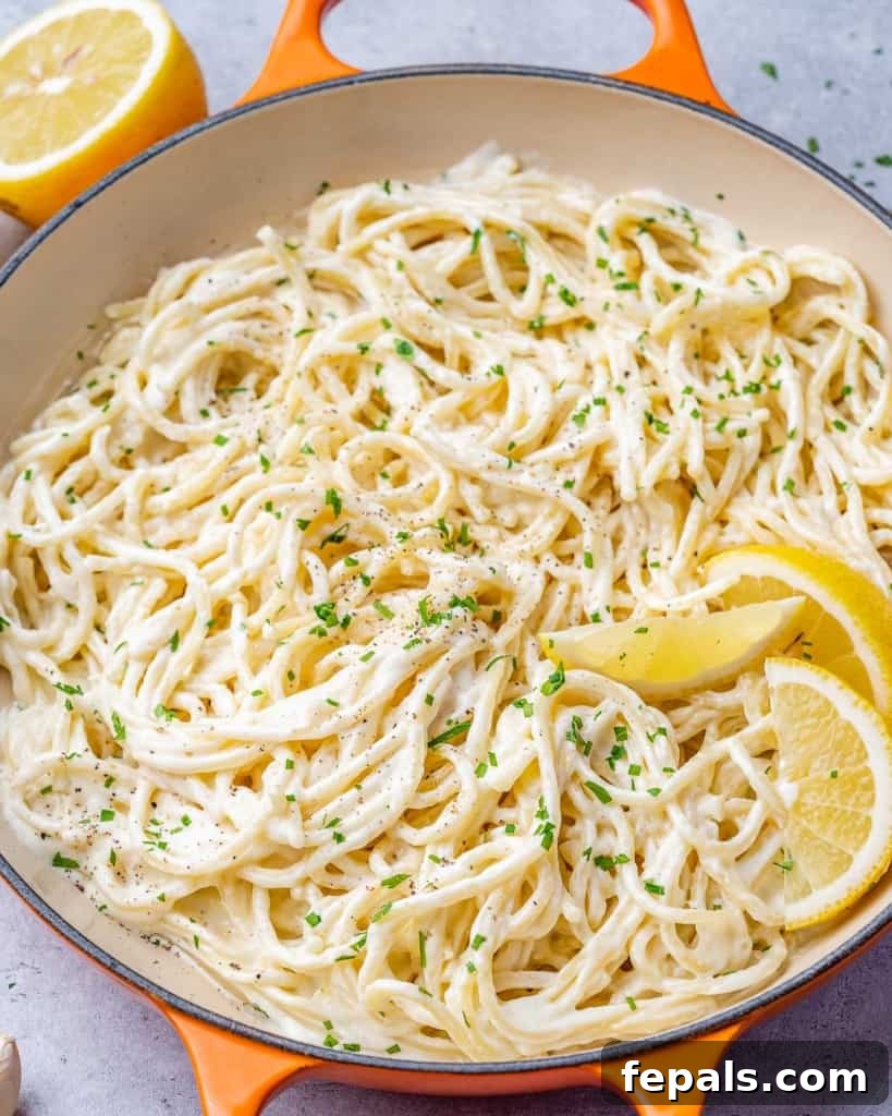 Luscious Vegan Lemon Pasta 3 Side shot of creamy pasta in a skillet with vibrant lemon wedges on the right side, showcasing its fresh appeal.