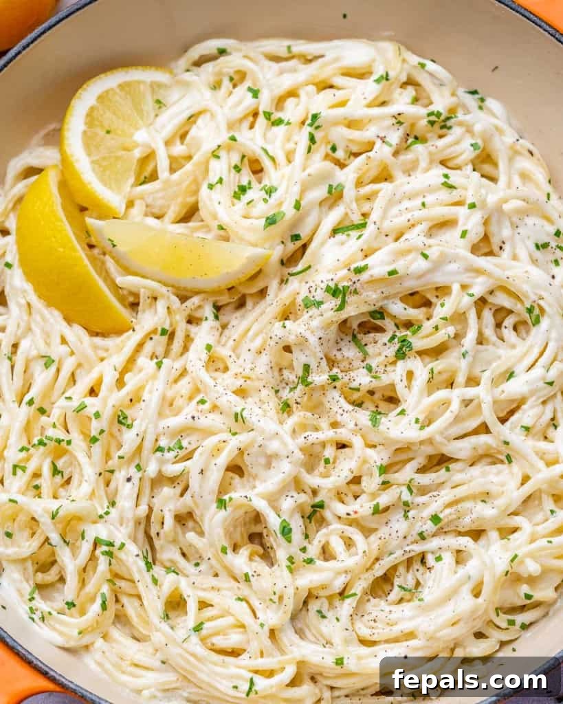 Luscious Vegan Lemon Pasta 10 Close up image of creamy pasta in a skillet with vibrant lemon wedges, emphasizing its rich texture and fresh garnish.
