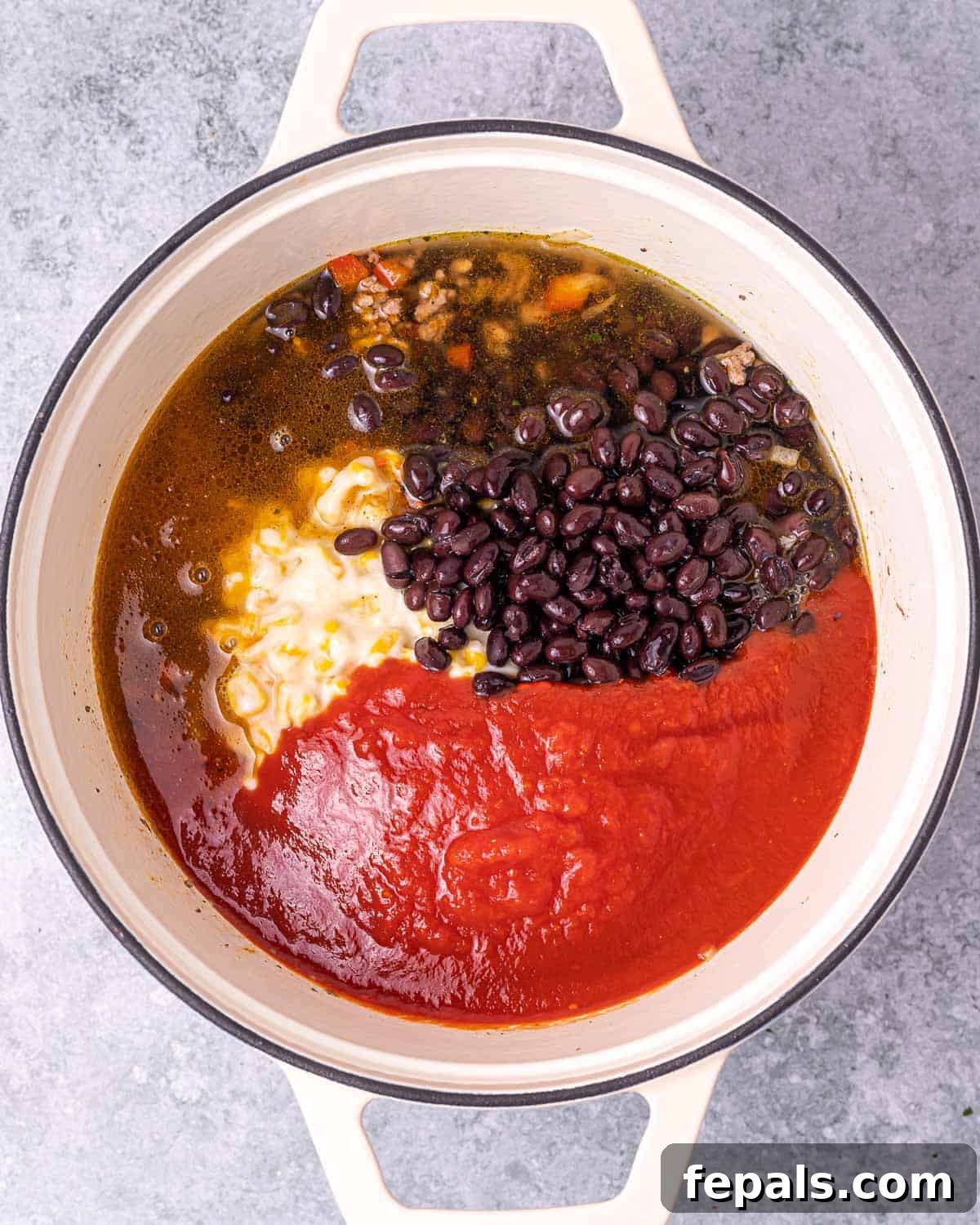 Southwest Creamy Beef Enchilada Soup 7 Pouring rich enchilada sauce and adding black beans to the soup pot with other ingredients.