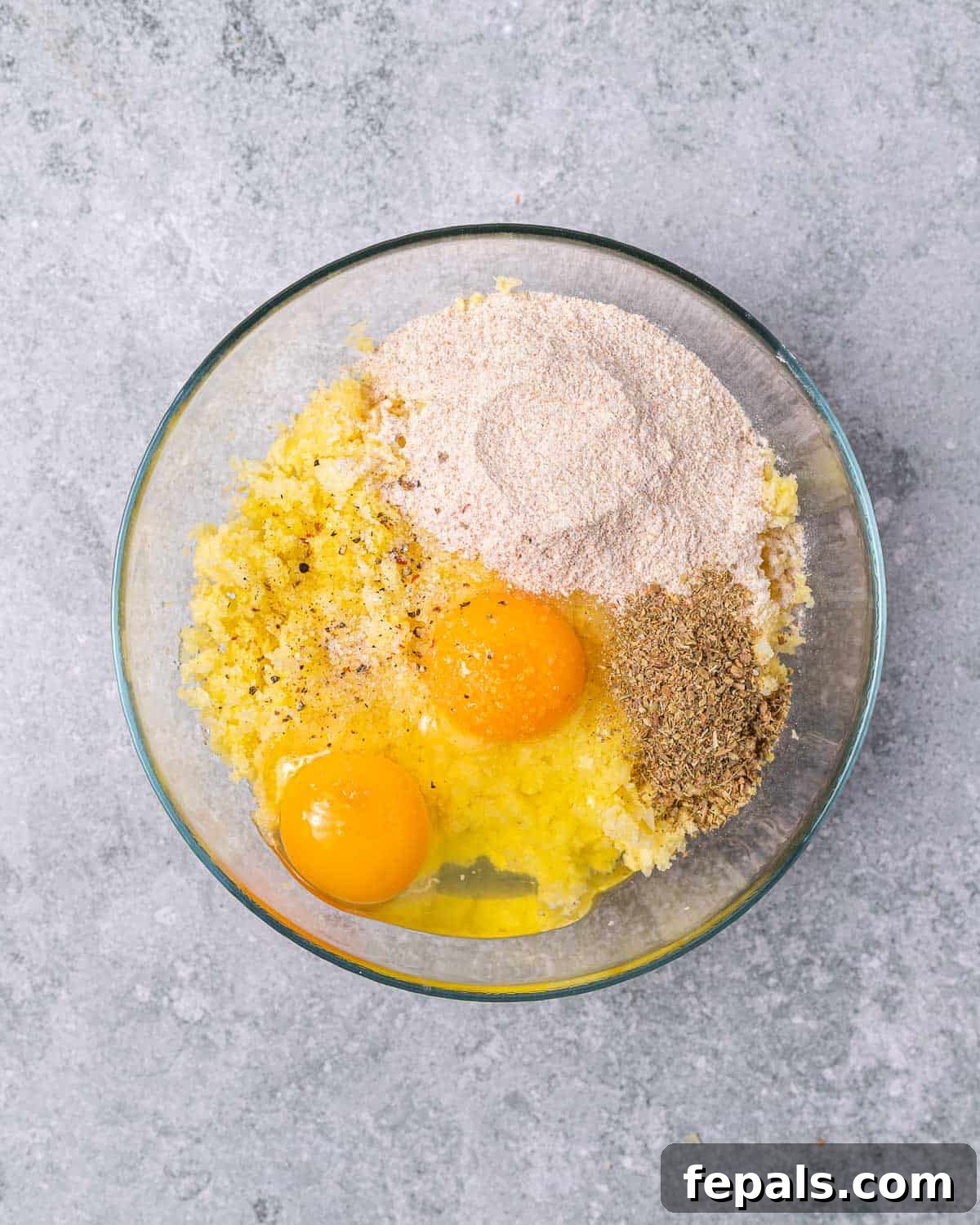 Timeless Golden Potato Fritters 8 Combining eggs, flour, and seasonings with minced vegetables in a bowl to make potato pancake batter.