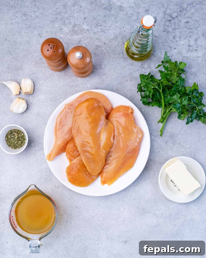 Uncooked chicken breasts, butter, broth, garlic and parsley on a counter.