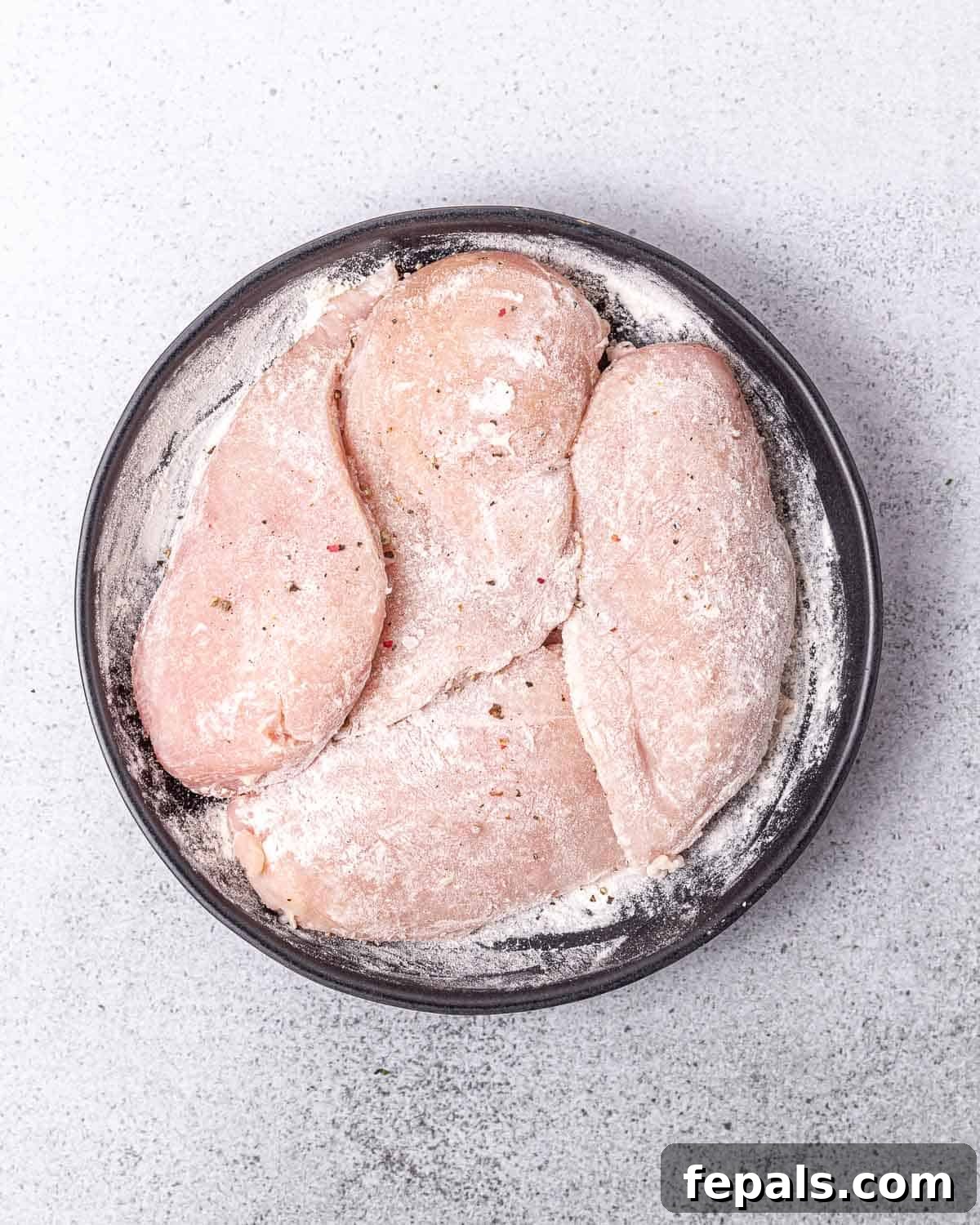 Velvety Ranch Chicken Delight 4 A hand is shown coating chicken breasts evenly in a bowl of flour seasoned with salt and pepper.