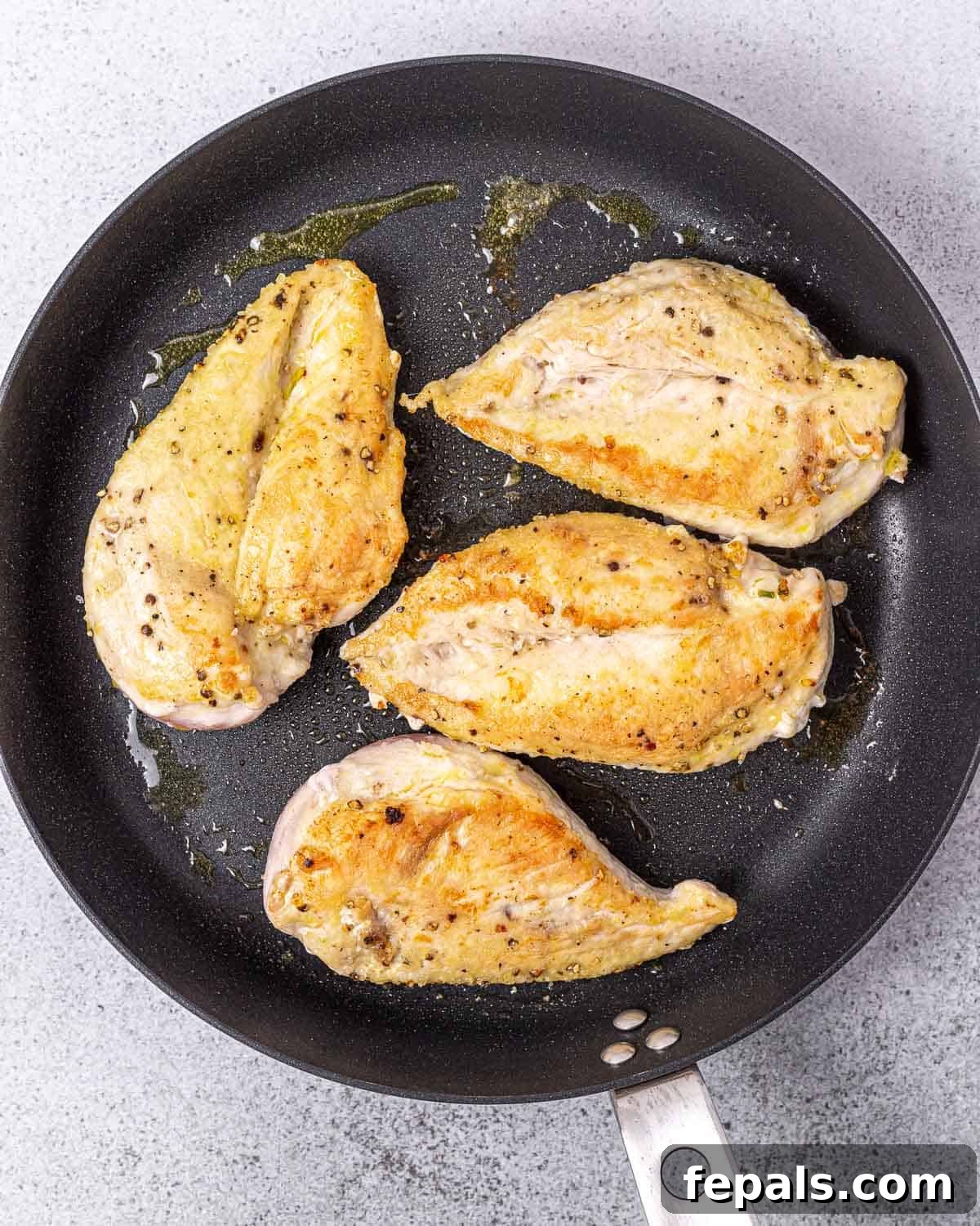 Velvety Ranch Chicken Delight 5 Two seasoned and floured chicken breasts are sizzling in a hot skillet with olive oil, developing a golden crust.