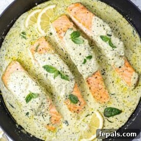 4 salmon fillets in a creamy pesto sauce in a black skillet.