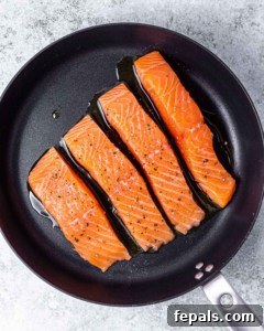 Salmon fillets cooking in a large skillet.