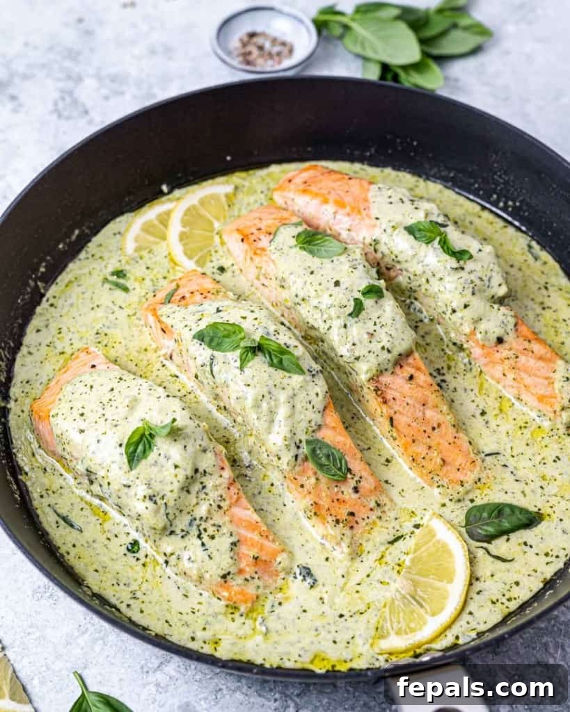 Close-up of salmon fillets gently simmering in a rich creamy pesto sauce in a skillet.