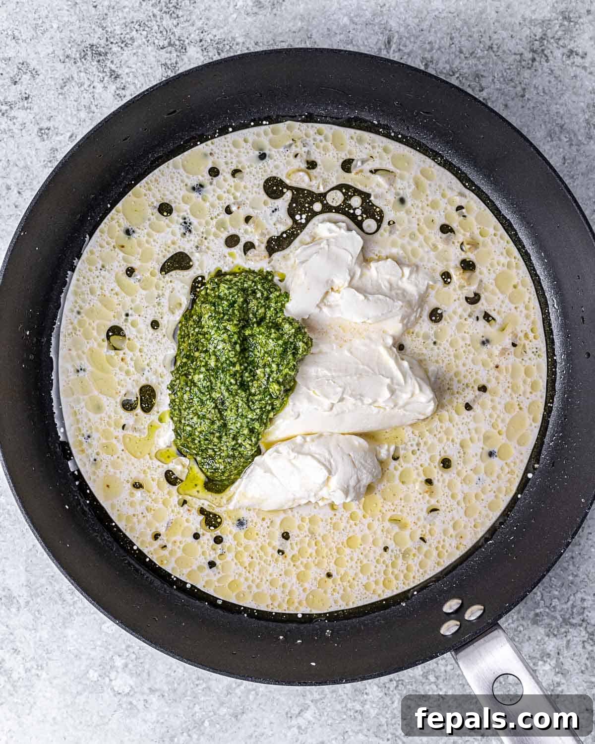 Almond milk, cream cheese, and pesto sauce being added to the skillet with garlic.