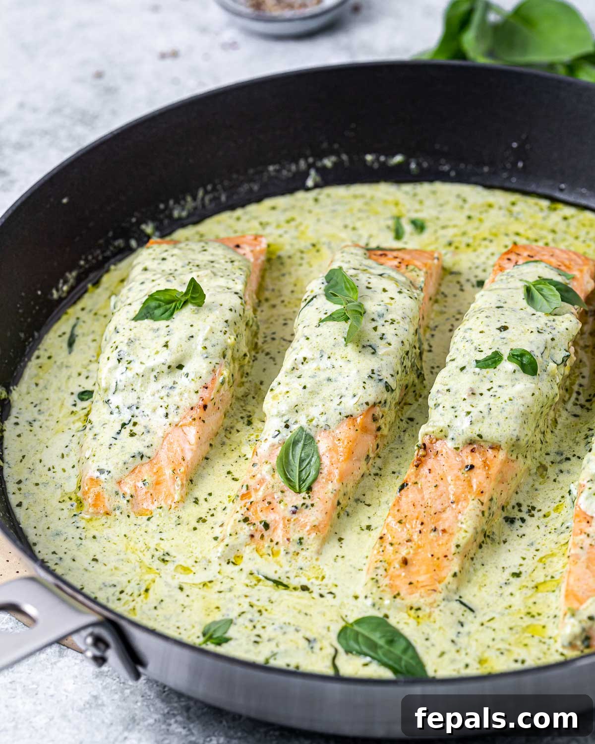 The seared salmon fillets returned to the skillet, coated in the creamy pesto sauce, ready to be served.