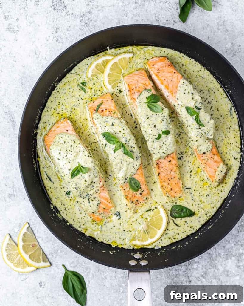 Overhead shot of creamy pesto salmon in a black skillet, perfectly cooked and glistening.