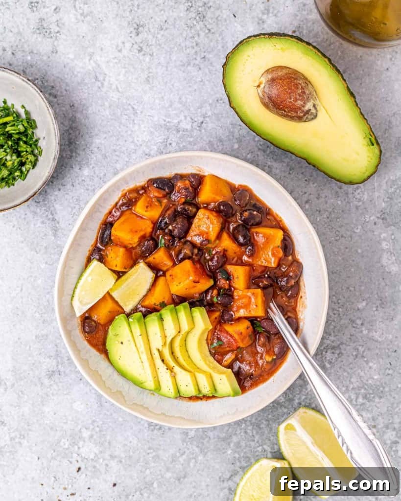 A spoon resting in a bowl of black bean sweet potato stew, with half an avocado elegantly placed in the top right corner, ready to be enjoyed.