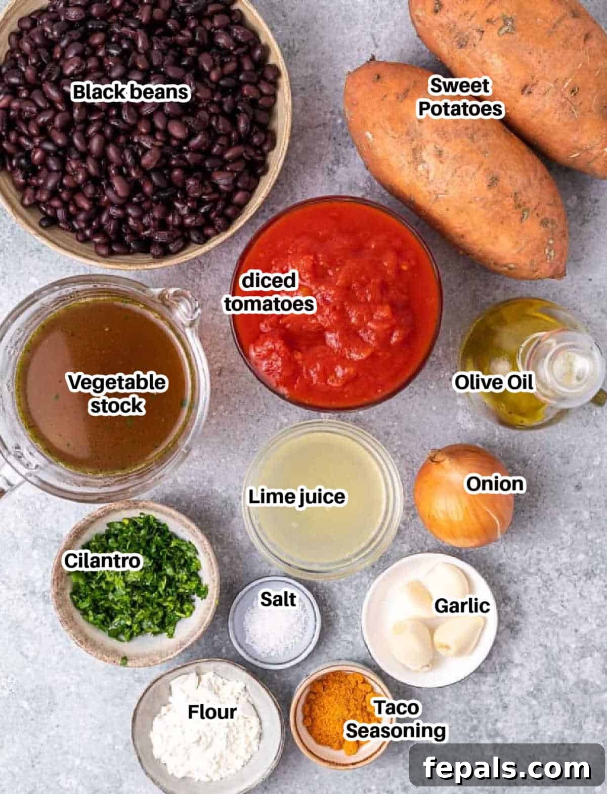 A vibrant selection of fresh ingredients laid out, including sweet potatoes, black beans, diced tomatoes, onions, garlic, and spices, ready to make sweet potato stew.