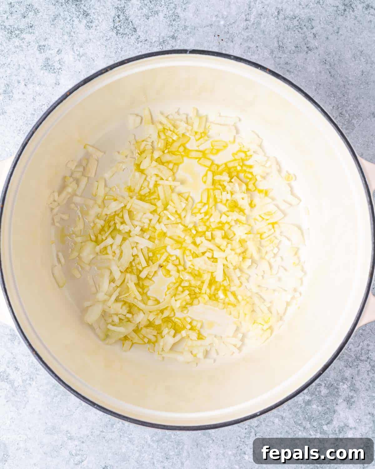 Sautéing diced yellow onion and minced garlic in olive oil in a large Dutch oven pot.
